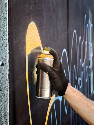Man sprays yellow graffiti on a dark wall outdoors