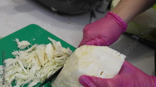 Culinary preparation shredding fresh Brassica oleracea cabbage with serrated knife. High angle close up shot captures rhythmic vegetable slicing process.