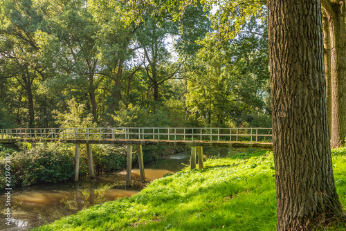 Narrow bridge for cyclists and pedestrians over a wide ditch. The photo was taken on a sunny autumn day in the outskirts of the Dutch city of Breda.