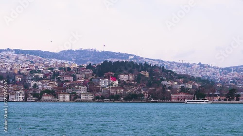 Scenic view of Istanbul and the Bosphorus Strait from a moving boat, with waterfront buildings, seagulls and a dramatic cloudy sky in the background.