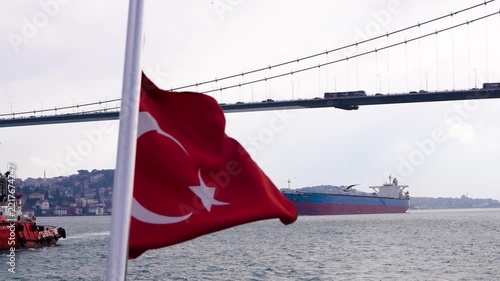Turkish flag waving from a boat cruising along the Bosphorus in Istanbul, with the Bosphorus Bridge, waterfront and city skyline in the background.