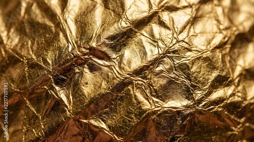 Crumpled gold foil texture background with metallic shine and intricate wrinkled patterns.