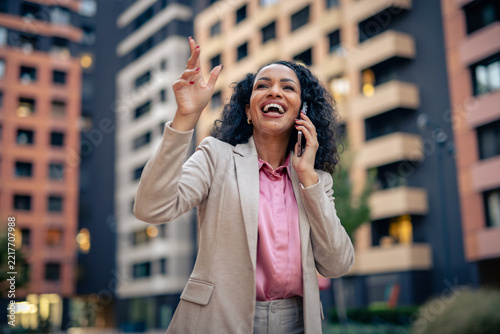 Excited professional woman laughing and gesturing during a phone call in the city, suggesting a successful deal, career achievement, celebration and victory