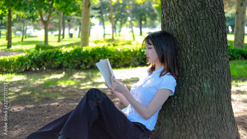 Beautiful Young Woman Reading Book While Leaning Against Tree Trunk in Park, Relaxing Girl Enjoying Literature in Green Nature Footage, Lifestyle Outdoor Leisure Concept Video, Peaceful Reading Scene