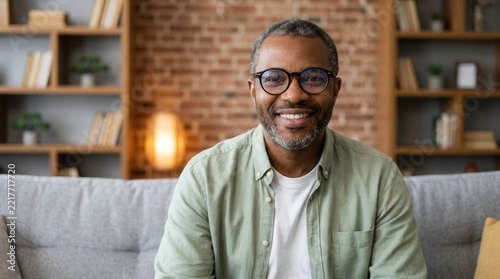 A cheerful adult African American man wearing glasses relaxes casually on a sofa.