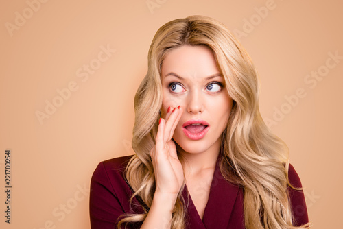 Portrait of concentrated big-eyed woman in classic outfit hiding mouth with palm whispering gossips, telling secret looking to the side with eyes isolated on yellow background