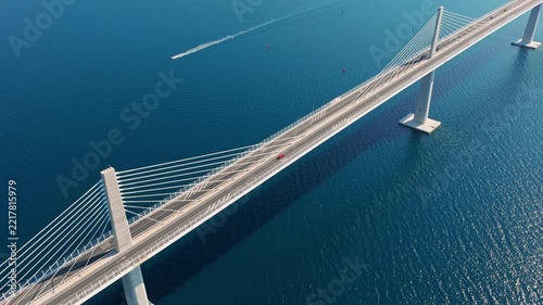 Drone shot of Pelješac Bridge spanning crystal blue waters, with boats gliding below. Bright daylight highlights modern architecture and sweeping coastal scenery from above.