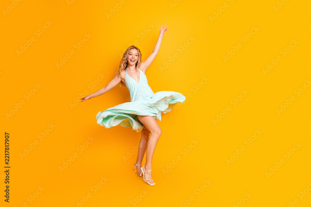 Fototapeta premium Happy young woman dancing in a mint dress on a bright yellow background, twirling and smiling to convey joy, summer fashion, movement and carefree confidence