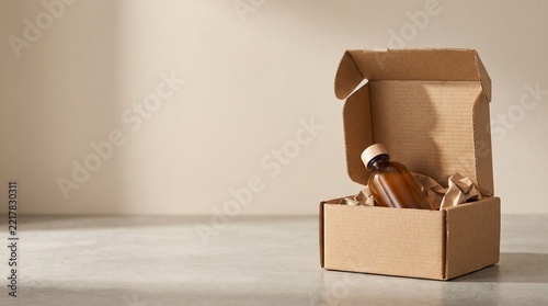 Open cardboard delivery box with a brown amber glass bottle inside, wrapped in eco-friendly paper packaging on a neutral background