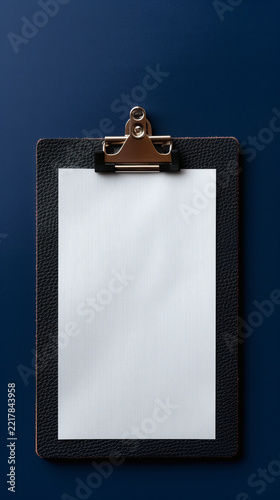 Dark leather clipboard with white paper sheet on blue background