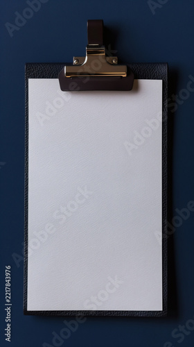 Leather clipboard with metal clip and white paper on dark blue surface