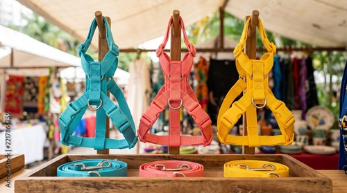 Colorful dog harnesses on hooks, Matching leashes at market stall, Bright outdoor pet accessory shopping, Clear buckles and stitched attachments, Woven fabric street retail display