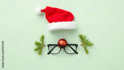 Creative santa claus face made from red christmas hat eyeglasses and green pine branches on mint green background
