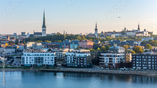 Aerial view of Tallinn Old Town skyline with St. Olaf's Church spire above modern seafront apartments in Kalaranna at golden hour, Estonia
