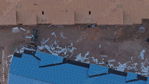 Aerial view of a construction site with blue roof underlayment, wooden framing, and scattered debris on dirt ground in Greeley, Colorado, United States.