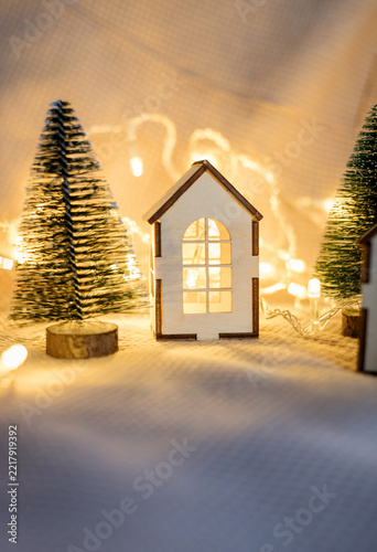 Miniature wooden toy house with Christmas trees and glowing lights.