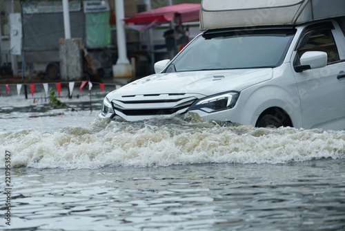 A vehicle is driving through deep floodwaters on the road.