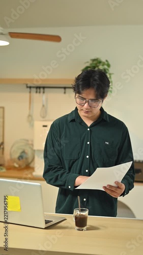Young Man Working on Laptop at Kitchen Counter with Coffee and Notebook