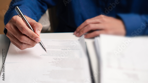 signature, Business professional reviews a contract with a pen at an office desk. Close-up legal paperwork concept for agreement, approval, compliance, corporate documentation and contract signing.