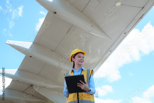 Female aviation engineer inspecting an aircraft wing while holding a tablet outdoors, representing aircraft maintenance, safety inspection, and aerospace technology.