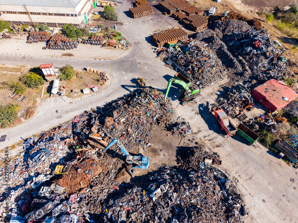 Fototapeta premium Heavy machinery operates at a scrap yard with piles of metal debris in an industrial area during the daytime