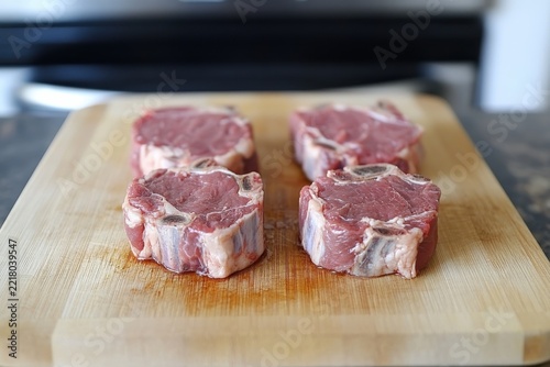 Four raw lamb chops on a wooden cutting board