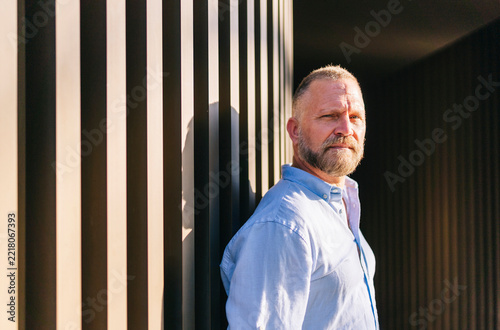 Middle aged man with beard standing by striped wall