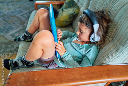 Boy With a Tablet and Headphones Lounging on a Green Sofa