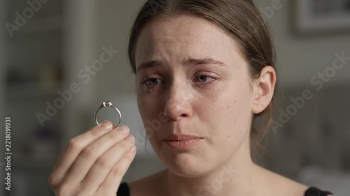 Sad young woman crying while holding broken engagement ring indoors