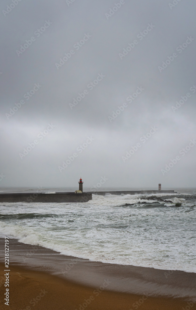 Fototapeta premium Stormy Atlantic ocean with powerful waves hitting coastline in Porto Portugal. Dramatic seascape with dark clouds, rough sea and coastal pier during bad weather conditions.