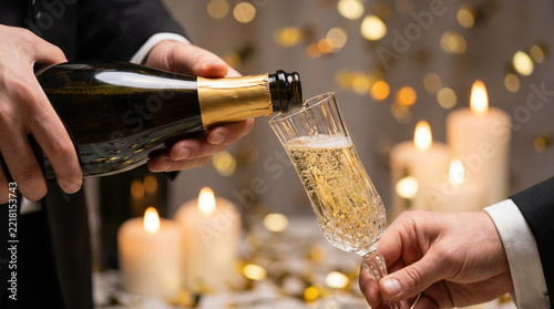 Crystal glassware receiving sparkling wine pour marks joyful toast during luxury party where waiter in tuxedo pours fizzy champagne against background with candle flames and festive bokeh.