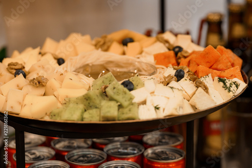 Assorted cheese platter with fruits nuts olives served on metal tray with drinks below at social gathering or party catering setup