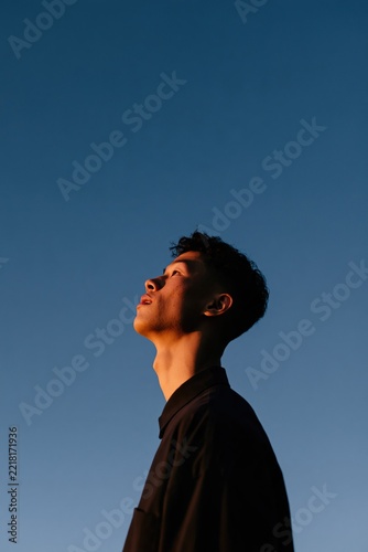 Young man profile portrait at dusk looking up against a clear blue sky for background banner or poster with dramatic warm side lighting