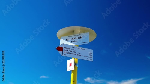 Close-up of a tourist directional wooden sign with arrows indicating hiking routes on a trail under a bright blue sky. 