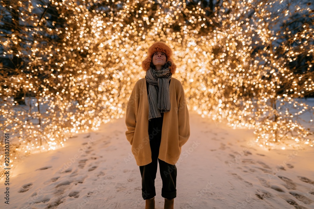 Fototapeta premium Individual under dense holiday light tunnel in snow for winter banner and festive background with warm glowing decorations and street scene