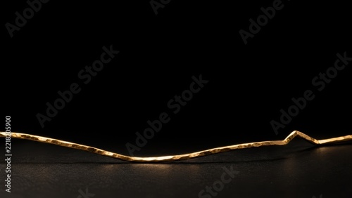 Minimalist gold metal wire isolated on a dark black background surface design