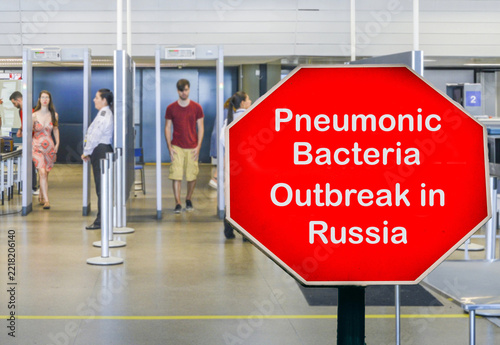 Airport security checkpoint with a red warning sign reading Pneumonic Bacteria Outbreak in Russia in October 2026