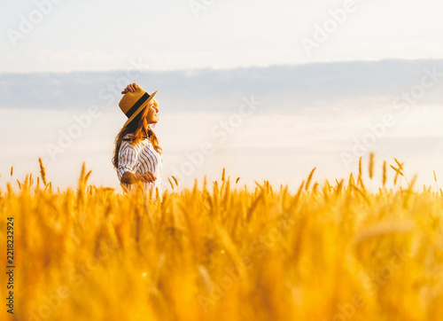 Obraz na plátně Carefree woman standing in a countryside wheat field during summer golden hour