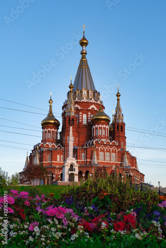 Red brick Russian Orthodox cathedral with golden onion domes and flower garden, Izhevsk, Russia