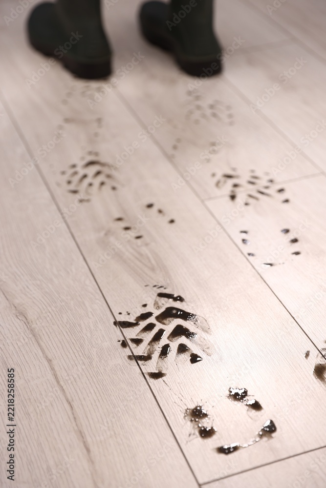 Fototapeta premium Woman in rubber boots leaving muddy footprints on wooden floor, selective focus