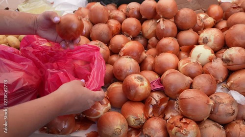 Customer Selecting Fresh Onions at a Market and Filling a Bag