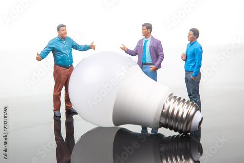 Miniature people discussing near a large light bulb in a studio setting