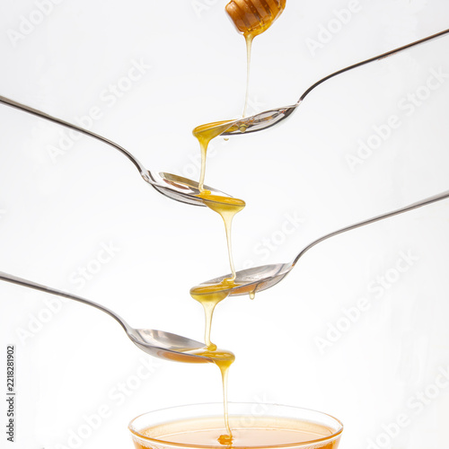 Honey drips from one spoon to another in a creative arrangement over a glass bowl