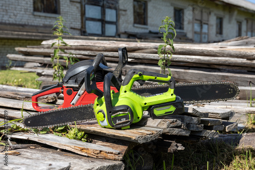 Obraz na plátně Green cordless electric chainsaw and red gasoline chainsaw lying on pile of old