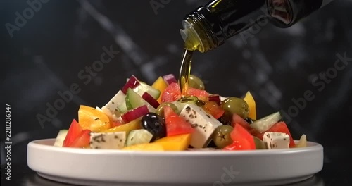 Olive oil pouring onto fresh greek salad with feta cheese olives tomato and cucumber in slow motion