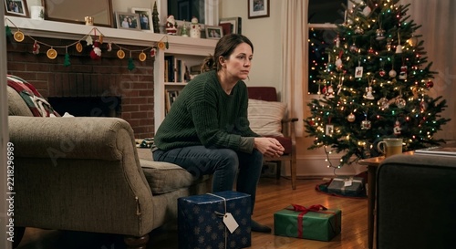 Sad woman sitting near wrapped presents by christmas tree at home