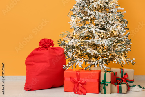 Christmas tree and Santa bag with gift boxes near yellow wall in room
