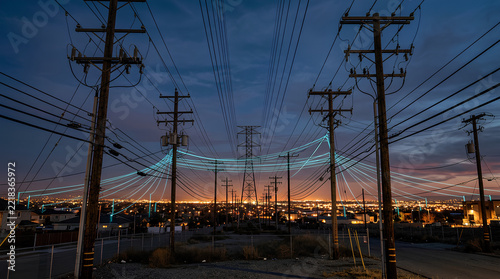Urban power line network at dusk with multiple utility poles and cables stretching across a cityscape under darkening sky