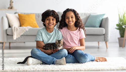Smiling boy and girl sitting on rug holding small kitten