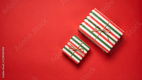 Two gift boxes wrapped in festive red, white, and green striped paper with rustic twine bows, arranged on a vibrant solid red background